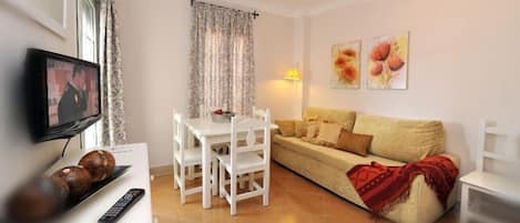A living room with a TV, white furniture, a sofa, and a dining table.