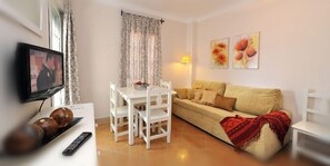Una sala de estar con televisor, mobiliario blanco, un sofá y una mesa de comedor.