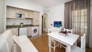 A compact living space with a kitchenette, a washing machine, a dining area with a table and chairs, and a television. - Aptos Leo San Bruno I Ii (Ayamonte)