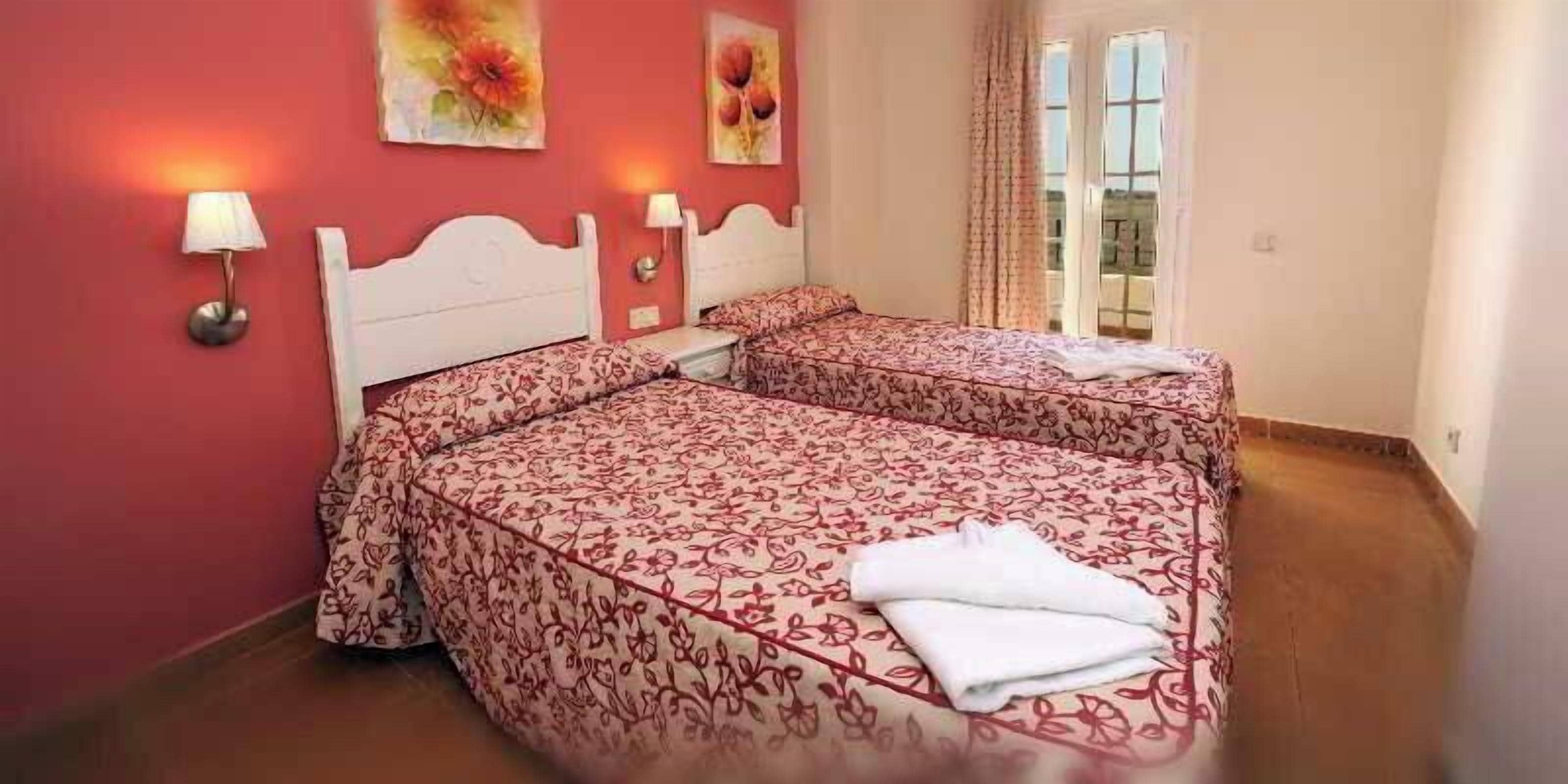 Un dormitorio con dos camas, una ventana con cortinas y lámparas fijadas a la pared.