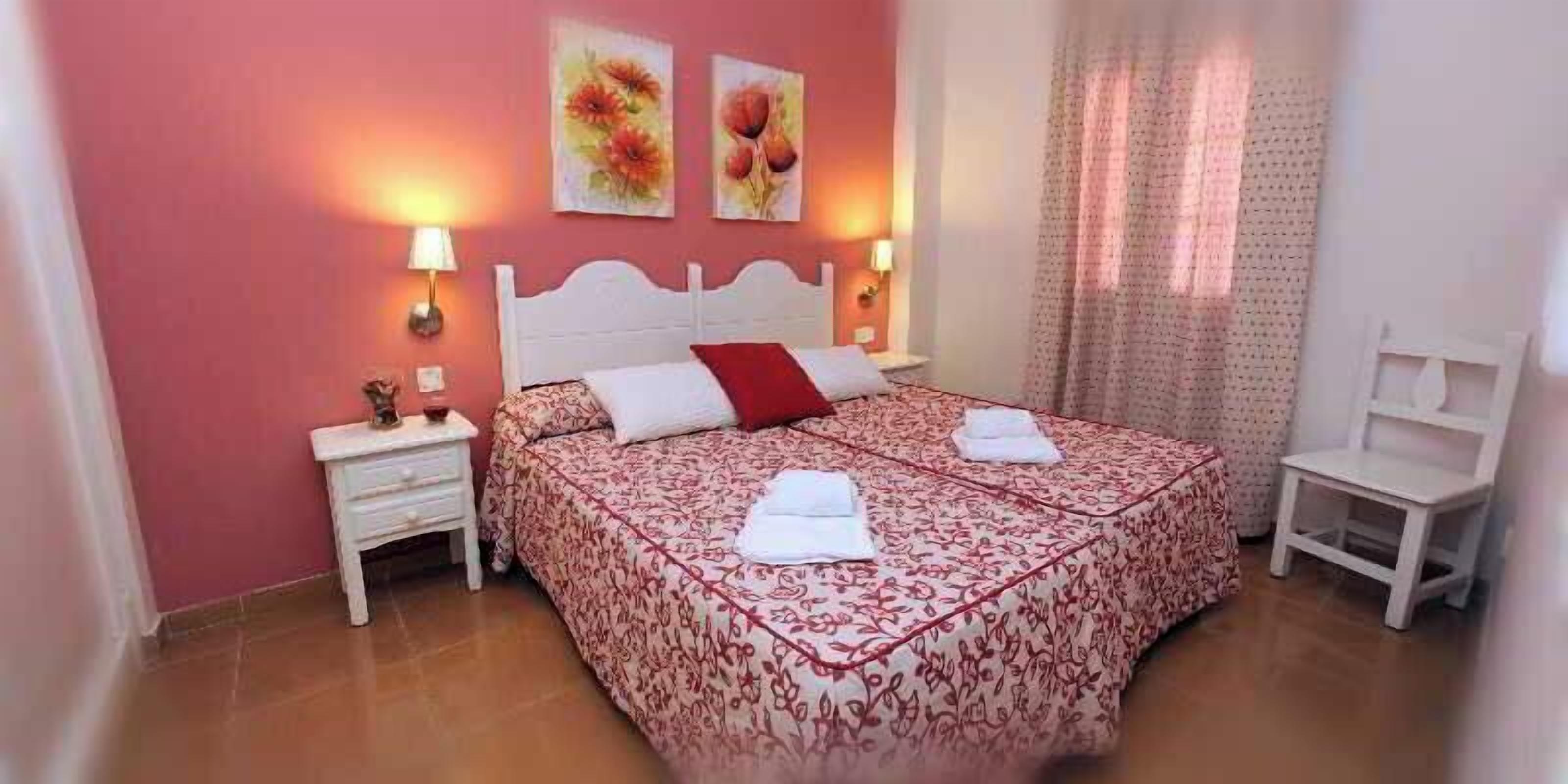 Um quarto com cama, mesas de cabeceira, uma cadeira e obras de arte na parede.
