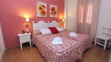 Um quarto com cama, mesas de cabeceira, uma cadeira e obras de arte na parede.