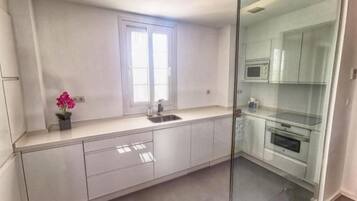 Una cocina moderna con separador de vidrio, armarios blancos y un ventanal que aporta luz natural.