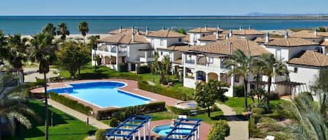 A resort with a swimming pool, multiple buildings, and a view of the sea.