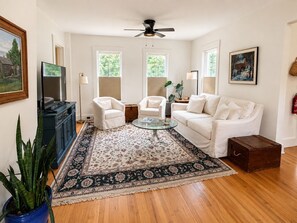 A living room with a sofa, two armchairs, a coffee table, a television, and a ceiling fan. - Riverfront 1800s Farmhouse, Sleeps 12+, Minutes from Killington + Woodstock (Bridgewater)