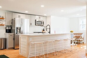 A modern kitchen with a central island, bar stools, and a dining area with a table and chairs. - Riverfront 1800s Farmhouse, Sleeps 12+, Minutes from Killington + Woodstock (Bridgewater)