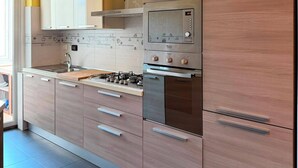 A modern kitchen with wooden cabinets, stainless steel appliances, and a tiled backsplash. - Apartment located in a prime location in Ostia Lido (Lido di Ostia)