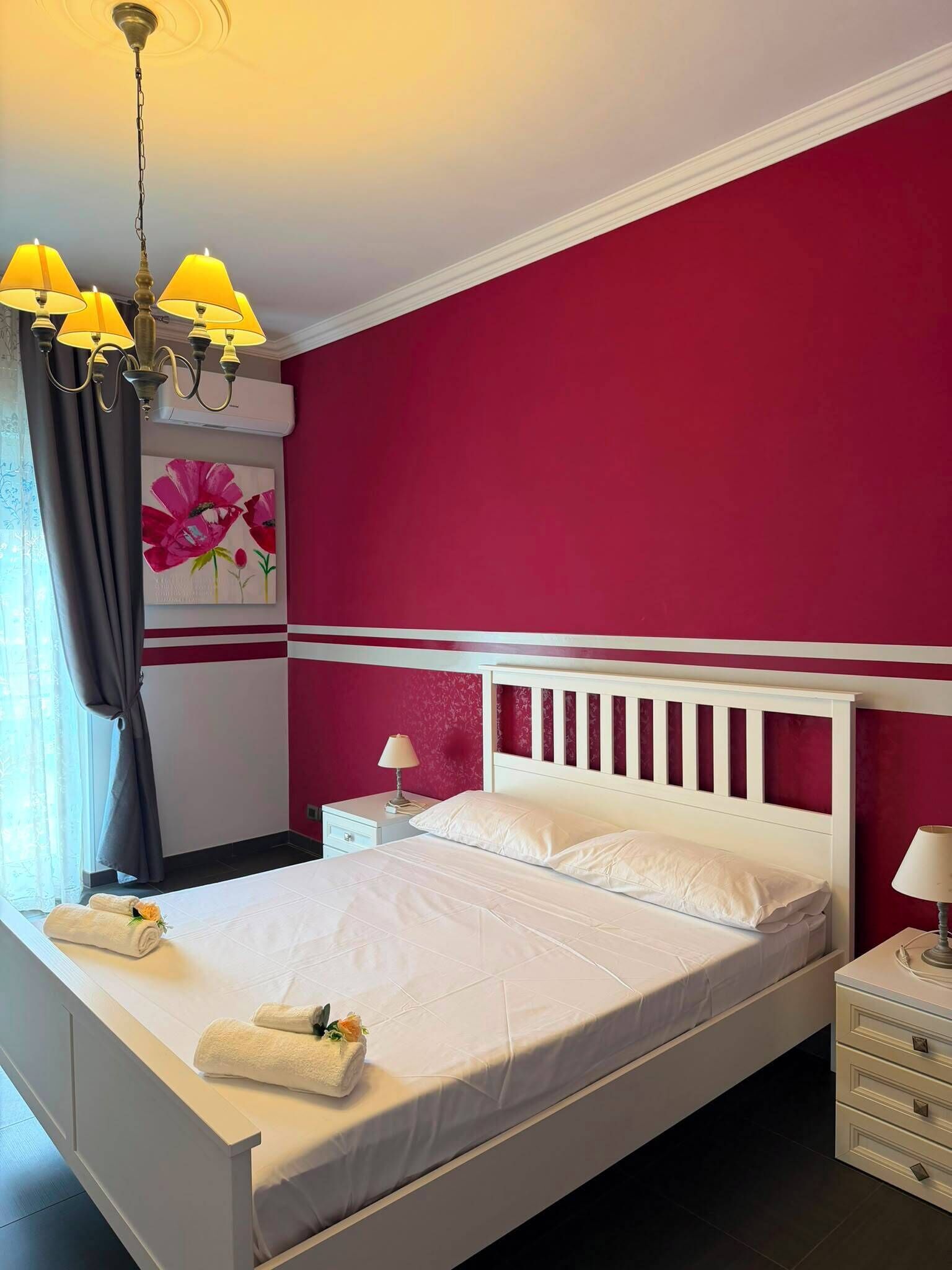 A hotel room with a bed, a nightstand, a lamp, a painting, and a chandelier.