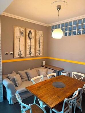 A dining area with a wooden table, white chairs, a sofa with cushions, and a wall with framed artwork. - Apartment located in a prime location in Ostia Lido (Lido di Ostia)