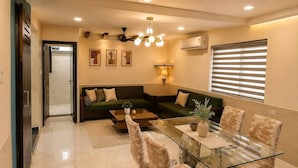 A modern living room with a glass dining table, sofas, and a ceiling fan.