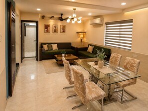 A modern living room with a glass dining table, sofas, and a ceiling fan. - 3BHK Luxury Villa (Thane)
