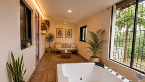 A modern bathroom with a large bathtub, a window with a view of greenery, and a wooden floor.
