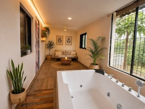 A modern bathroom with a large bathtub, a window with a view of greenery, and a wooden floor. - 3BHK Luxury Villa (Thane)