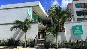 A modern building with a staircase leading to a balcony, surrounded by palm trees and a sign for 'Praiana Pousada.' - Pousada Praiana (Ipojuca)