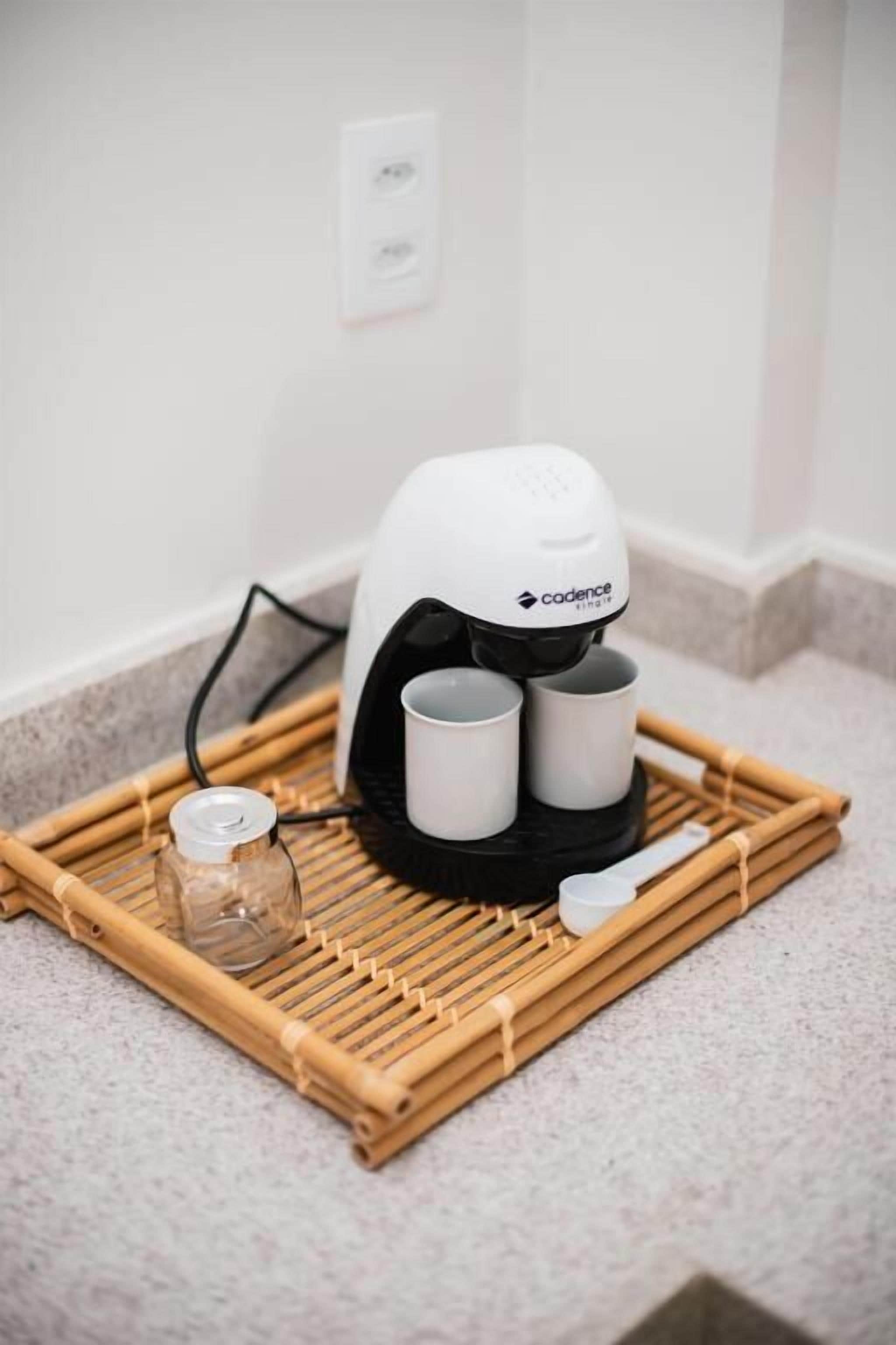 Una cafetera con dos tazas sobre una bandeja de bambú, un vaso y una cuchara en la encimera de una cocina.