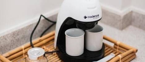 Una cafetera con dos tazas sobre una bandeja de bambú, un vaso y una cuchara en la encimera de una cocina.