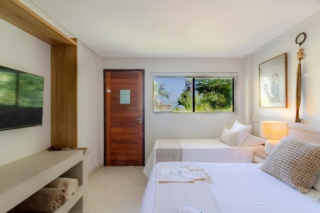 A hotel room with a bed, a desk, a chair, a window with a view of greenery, and a door.