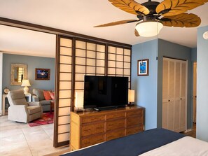 Ein Hotelzimmer mit einem großen Flachbildfernseher, einem Deckenventilator, einer hölzernen Kommode, einem Sofa und einem Schiebetürenschrank.