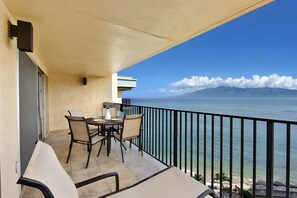 A balcony with a table set for two, overlooking a body of water with mountains in the distance. - Sunny 4BR, 2 Condos for 12 in Lahaina, Hawaii! (Lahaina)