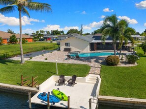 A residential area with a swimming pool, a dock with kayaks, and a well-maintained lawn. - Seaside Villa Paradise Point - large heated pool, wide canal, south facing, (Cape Coral)