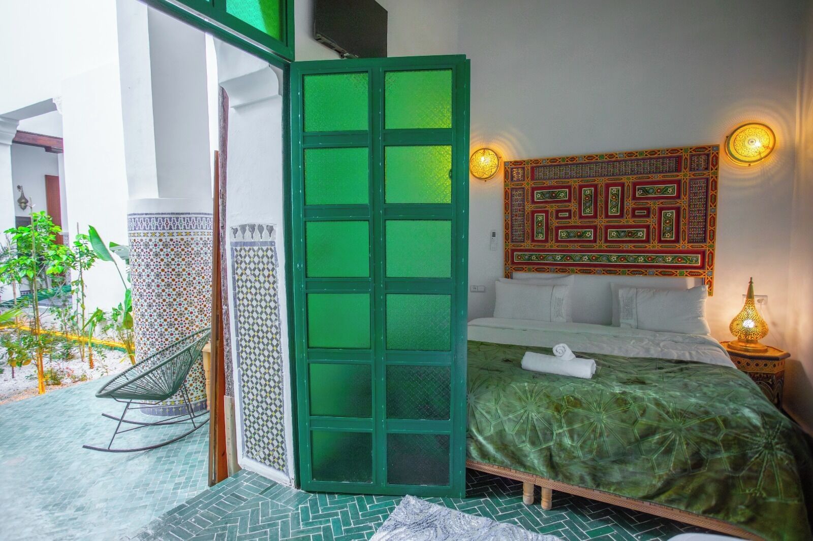 A bedroom with a green bedspread, a decorative wall hanging, and a nightstand with a lamp.
