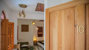 Una puerta de madera con una placa de latón con número, un piso con diseño y lámparas colgantes.