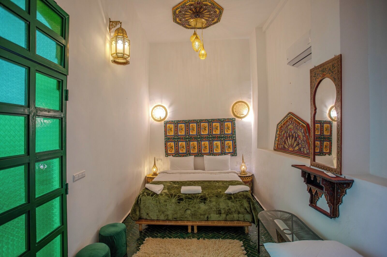 A room with a bed, decorative wall panels, a mirror, and a green-framed window.