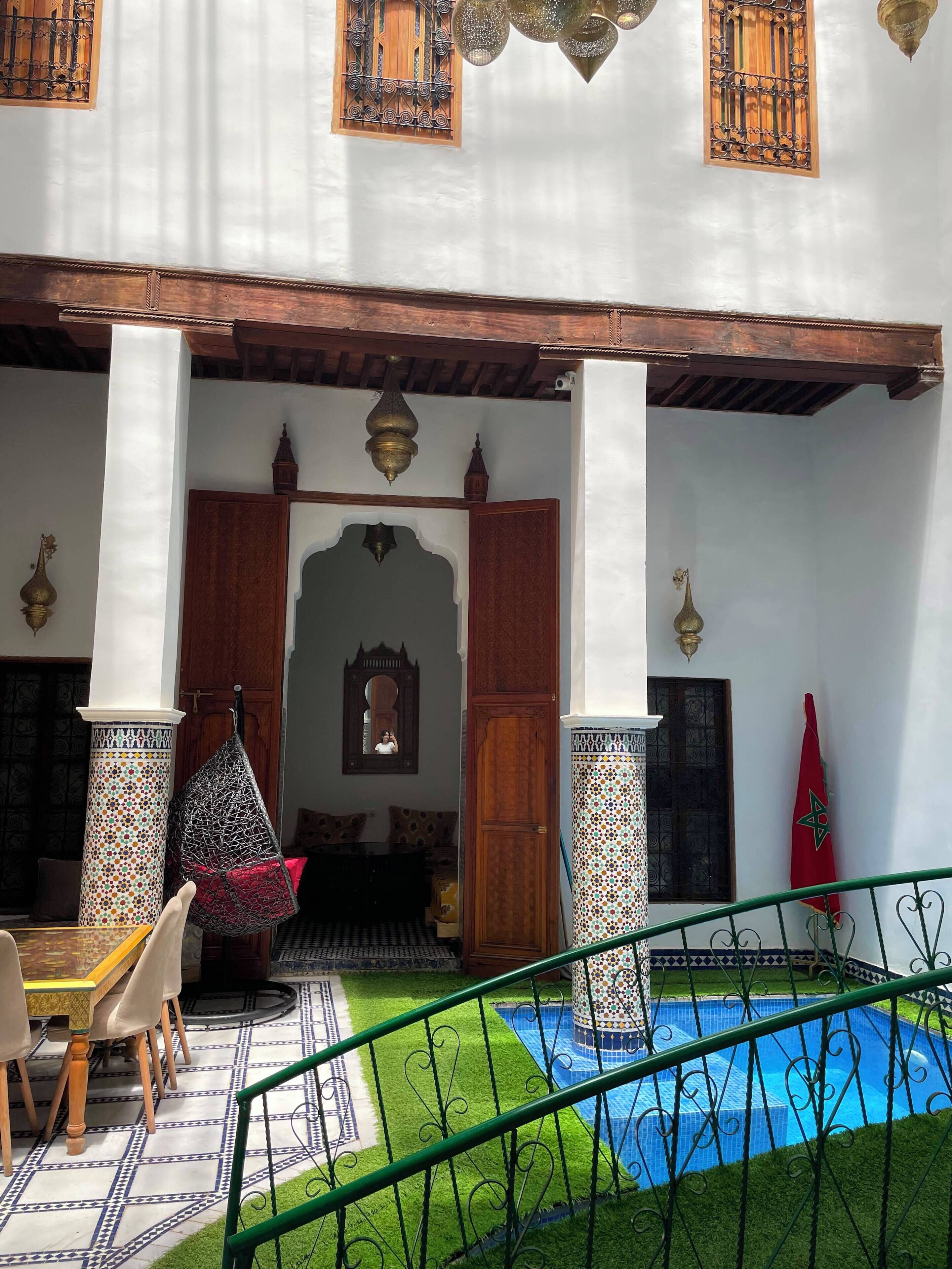 A courtyard with a pool, a dining area with chairs, and a flag.