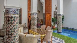 Un área de estar al aire libre con una mesa y sillas, rodeada de columnas decoradas y un suelo de baldosas.