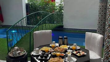 A dining area with a table set for breakfast, a pool in the background, and a staircase leading to a balcony.