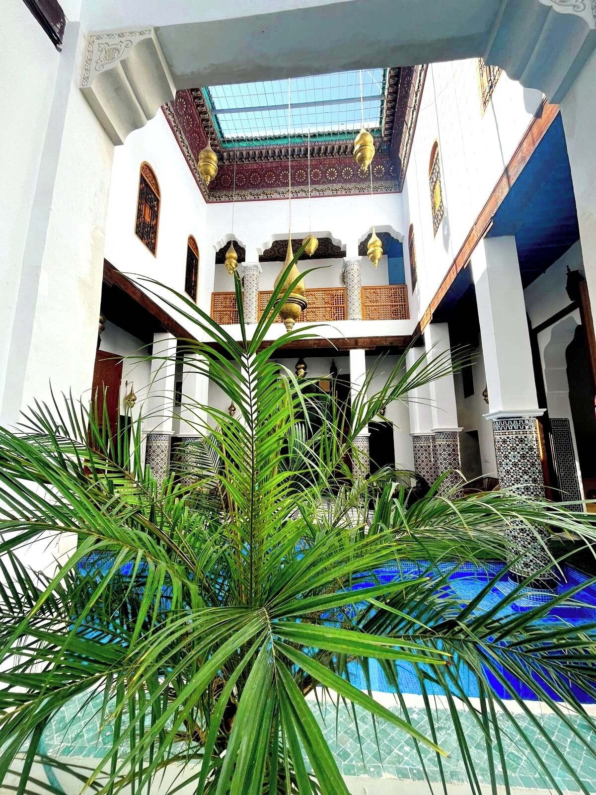 A courtyard with a pool, palm trees, and a building with a tiled roof and columns.