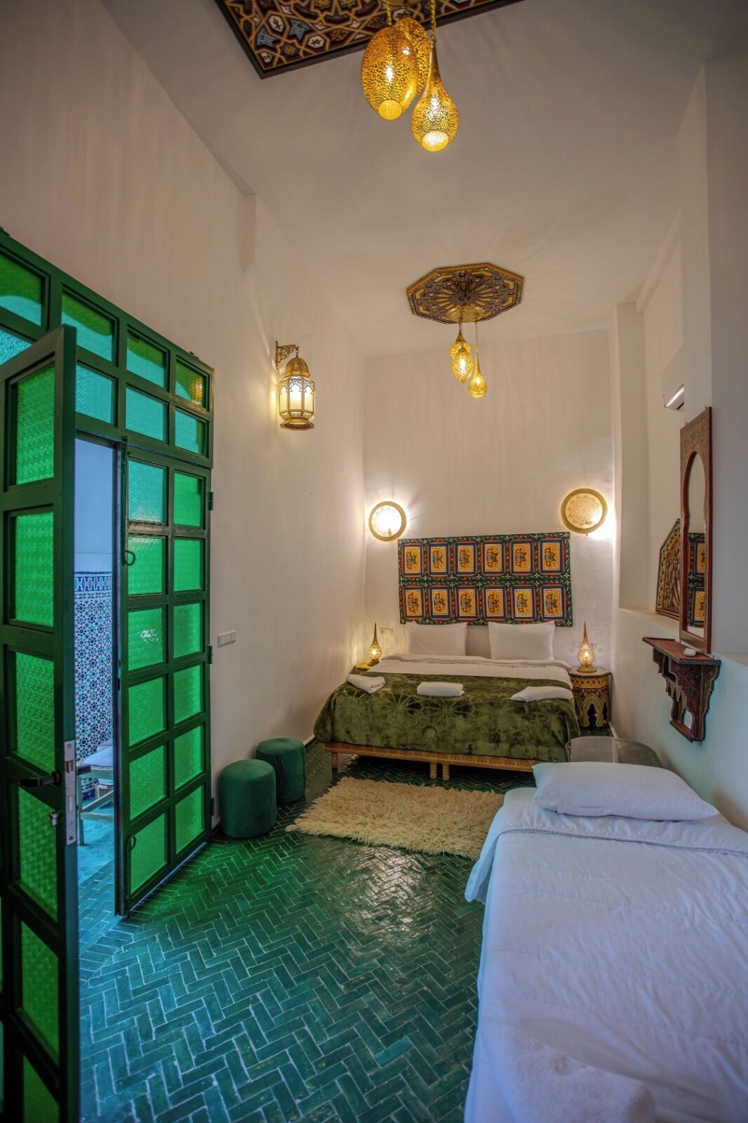 Um quarto com piso estampado em tons de verde, uma cama com roupa de cama branca, uma cabeceira decorativa e um lustre.