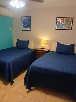 Quarto de hotel com duas camas, uma mesa de cabeceira, uma luminária e dois quadros na parede.
