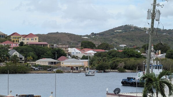 Uma vila costeira com casas, um cais e uma colina ao fundo.