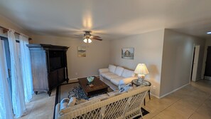 Ein Wohnzimmer mit einer Couch, einem Couchtisch, einem Fernseher, einem Deckenventilator und einer Lampe.
