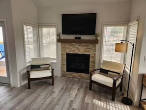 A living room with a fireplace, two armchairs, a television mounted above the fireplace, and a floor lamp. - The Lake Escape! (Lake Geneva)