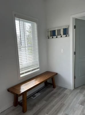 A room with a bench, a window with blinds, a door, and a wall-mounted shelf with hooks. - The Lake Escape! (Lake Geneva)