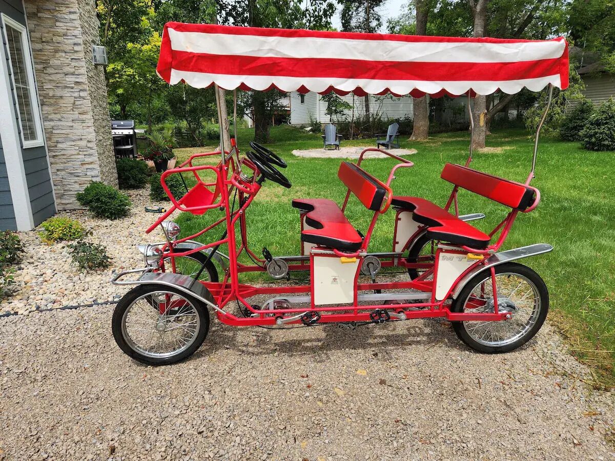 En rød og hvid cykel med to sæder, parkeret på en grusvej.