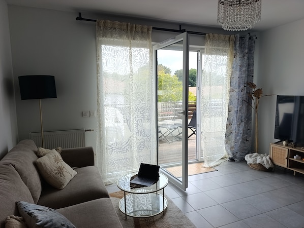 Una sala de estar con un sofá, una mesa de centro de vidrio, un televisor y un ventanal corredero que da a un área exterior.