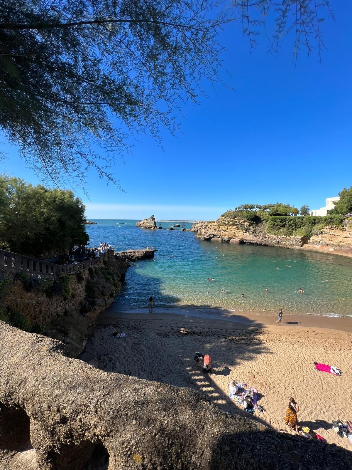 A coastal beach with clear water, rocky terrain, and a stone wall.