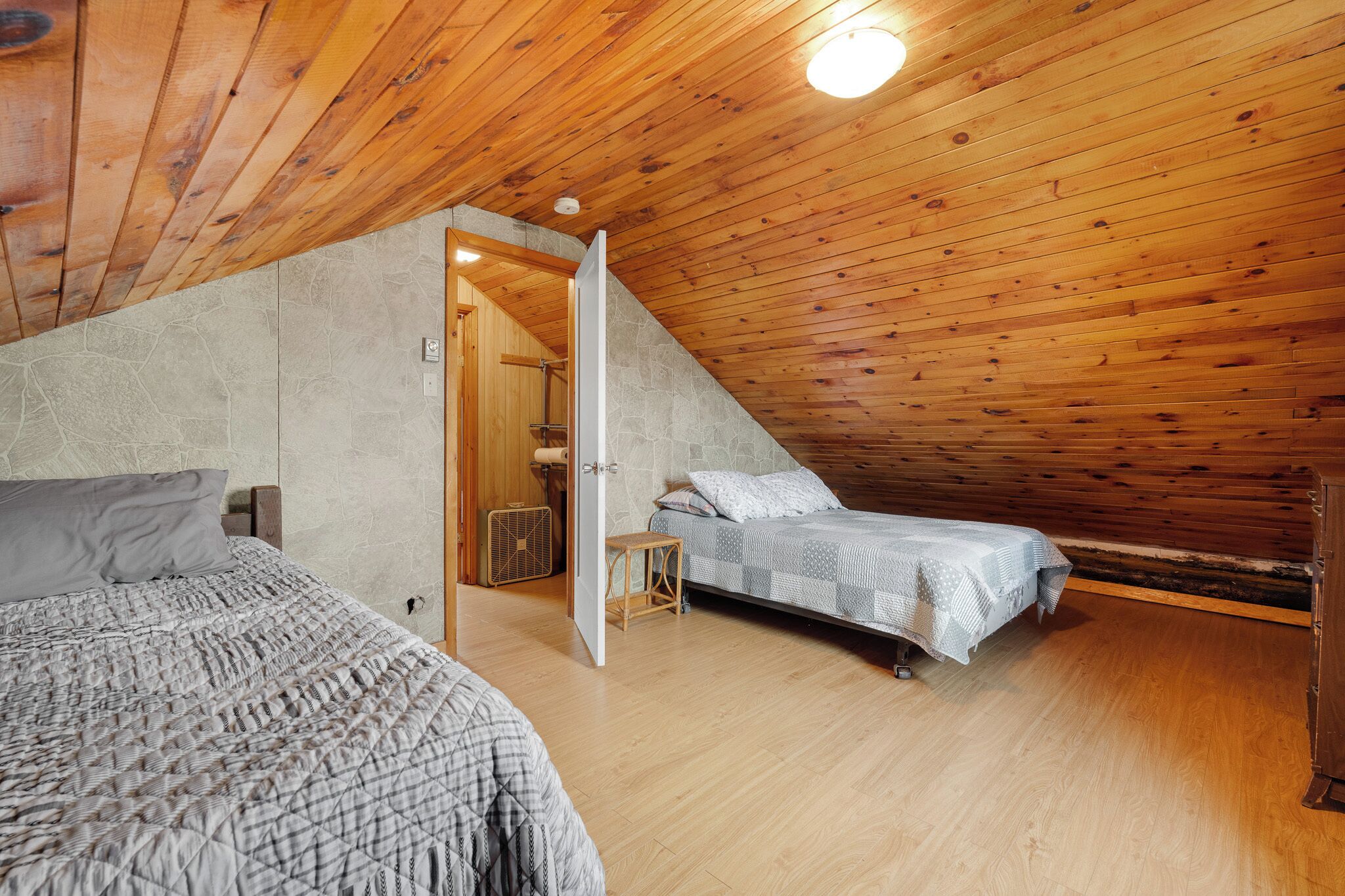A bedroom with a sloped ceiling, two beds, a wooden floor, and a stone wall.