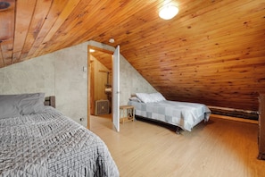 A bedroom with a sloped ceiling, two beds, a wooden floor, and a stone wall.