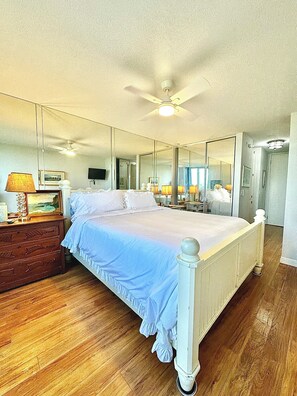 A bedroom with a bed, dresser, mirror, ceiling fan, and wooden flooring. - Northcoast Village Impeccable Unit with both Ocean and Harbor Views (Oceanside)