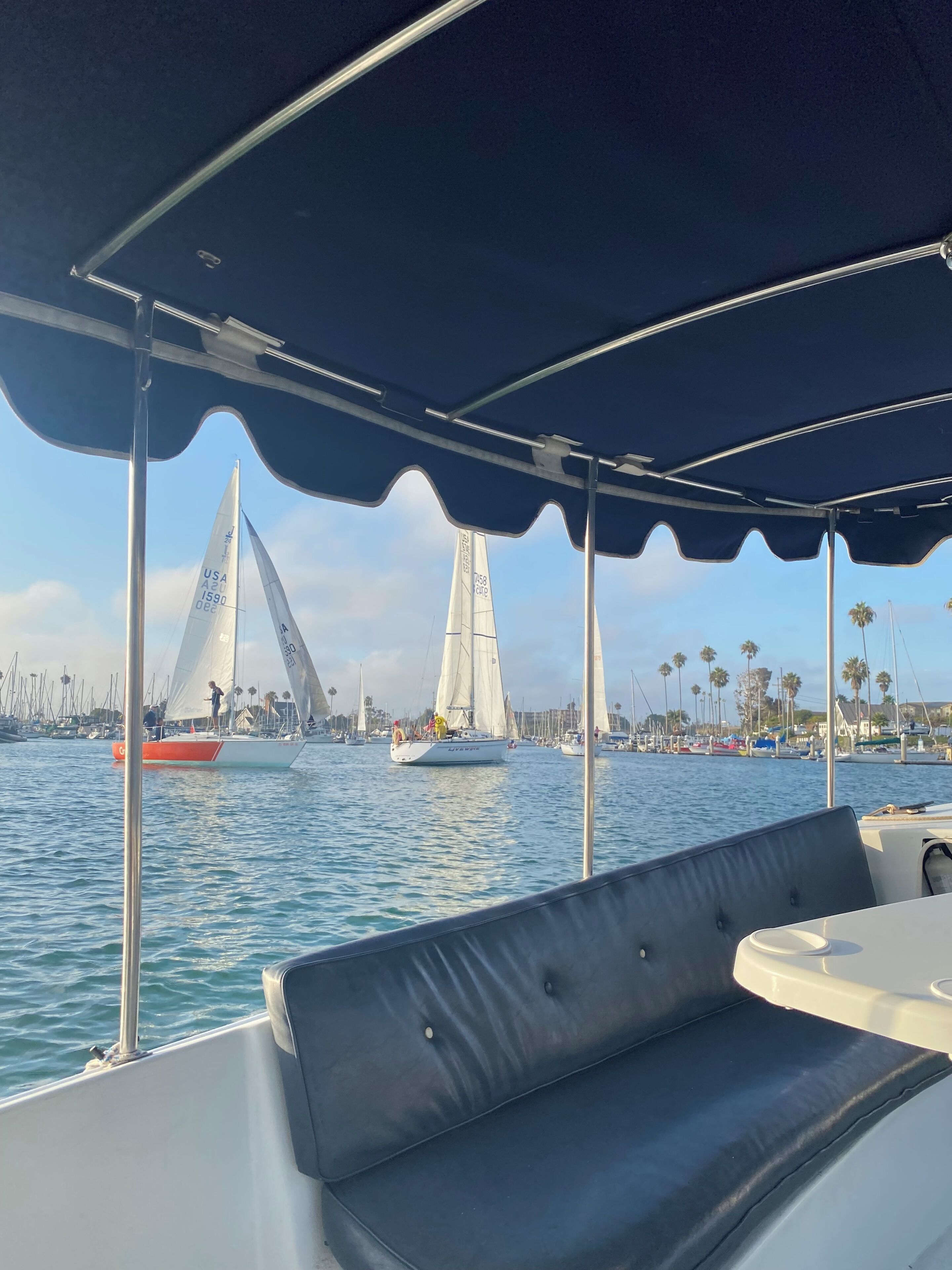 Barco com área de estar coberta e vista para veleiros ao fundo.