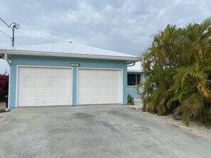 A two-story building with a garage, a blue exterior, and a palm tree in the foreground. - Waterfront Canal Priv Home. 3BD, 2BA, Pool, Kayak+Cabana Club! 70' Seawall-KCB (Marathon)