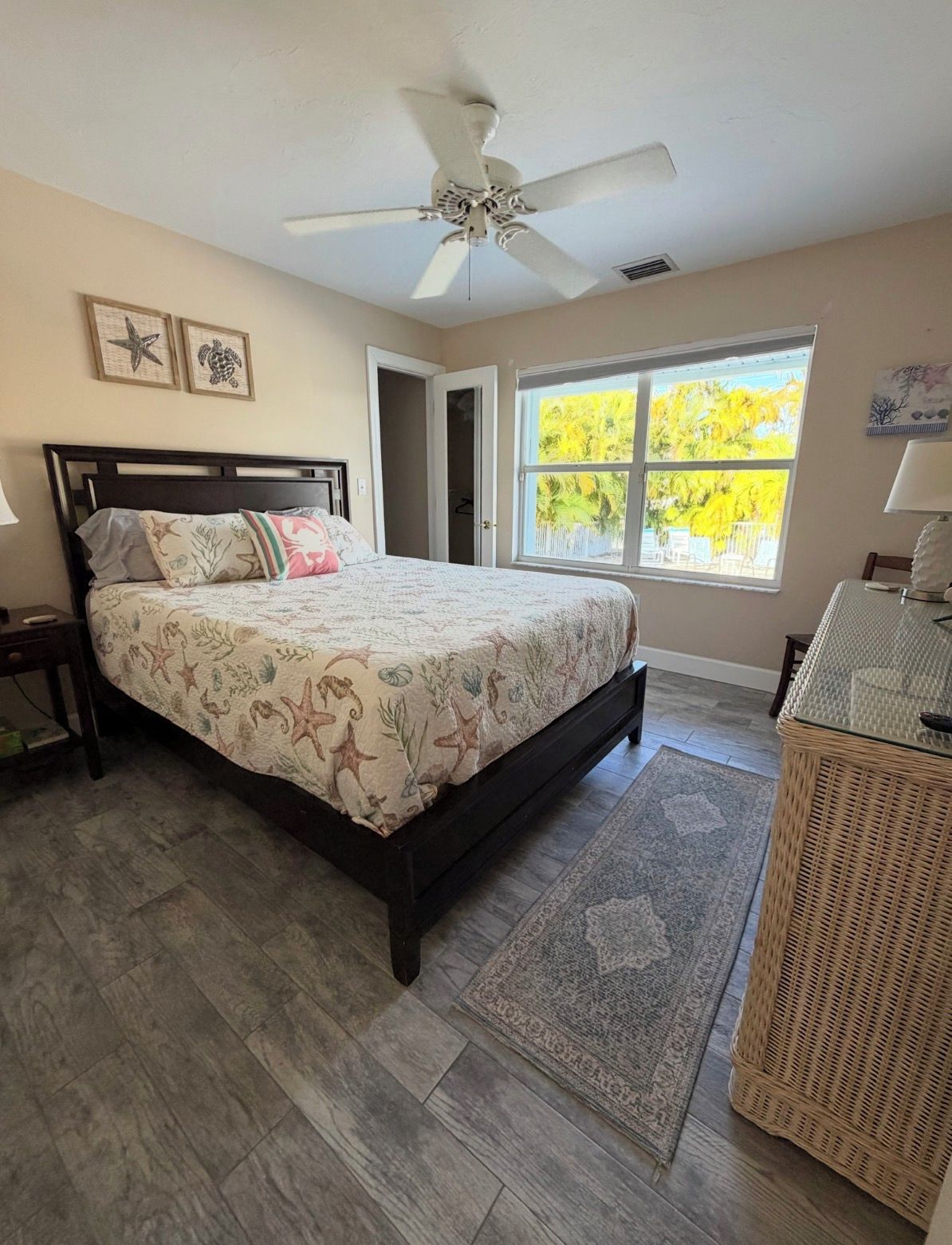 Un dormitorio con cama, ventilador de techo, ventana con vistas y una silla de mimbre.