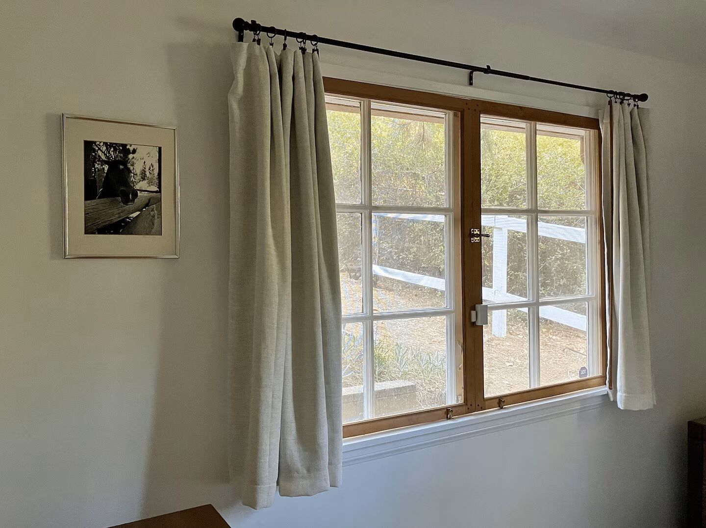 A room with a large window, a curtain rod, and a framed picture on the wall.