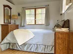 A bedroom with a bed, a dresser, a mirror, a window with curtains, and a bedside table with books.