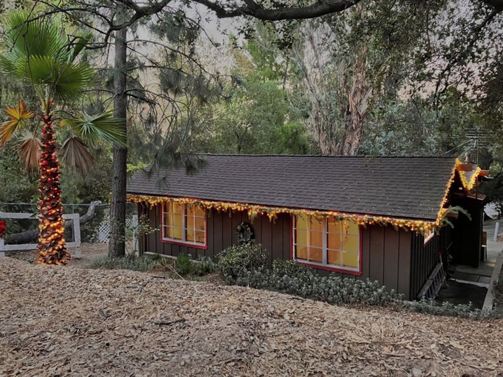 A small wooden cabin with a sloped roof, surrounded by trees and a wooden fence.