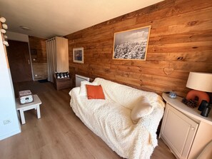 Ein gemütliches Zimmer mit Holzwand, einem weißen Sofa, einem kleinen Tisch und einem Schrank.